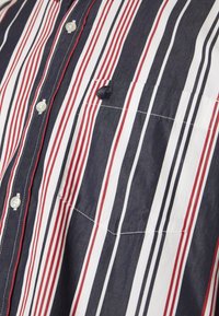 Gestreept shirt in marineblauw, rood en wit. Voorzien van knopen en een borstzak met een contrasterende donkere knop. Glad stofgevoel.