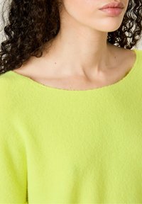 Neon groene, zachte gebreide trui met een wijde halslijn en een lichte textuur. De stof lijkt iets harig, wat het comfort benadrukt.