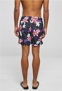 Fekete fürdőshorts élénk virágmintával, mely pink és zöld virágokat tartalmaz, rugalmas derékpánttal és oldalsó zsebekkel.