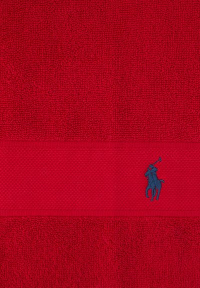 Rødt tekstureret håndklæde med et vandret vævet bånd, der har en lille blå broderet polospiller til hest.