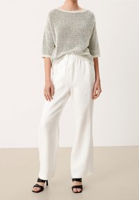 Lekki, teksturowany sweter z dzianiny, z szerokim dekoltem, w połączeniu z luźnymi białymi spodniami z lnu i czarnymi sandałkami na obcasie.