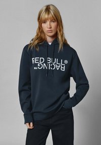 Sudadera negra con "RED BULL RACING" en letras grandes blancas. Cuenta con capucha con cordón y puños acanalados. Tela suave, corte holgado.