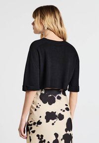 Maglione nero corto con maniche ampie, colletto a coste e polsini arrotolati, abbinato a una gonna fantasia nei toni del beige, nero e bianco.