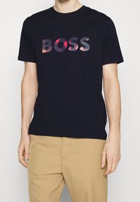 Marinblå bomullströja med en stor, texturerad "BOSS"-logotyp i en färgglad, gradientdesign. Klassisk rund halsringning och korta ärmar.