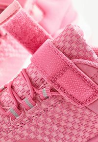 Chaussures de sport roses avec un design en maille texturée, une bande velcro ajustable et des lacets élastiques. Construction légère avec une finition douce.