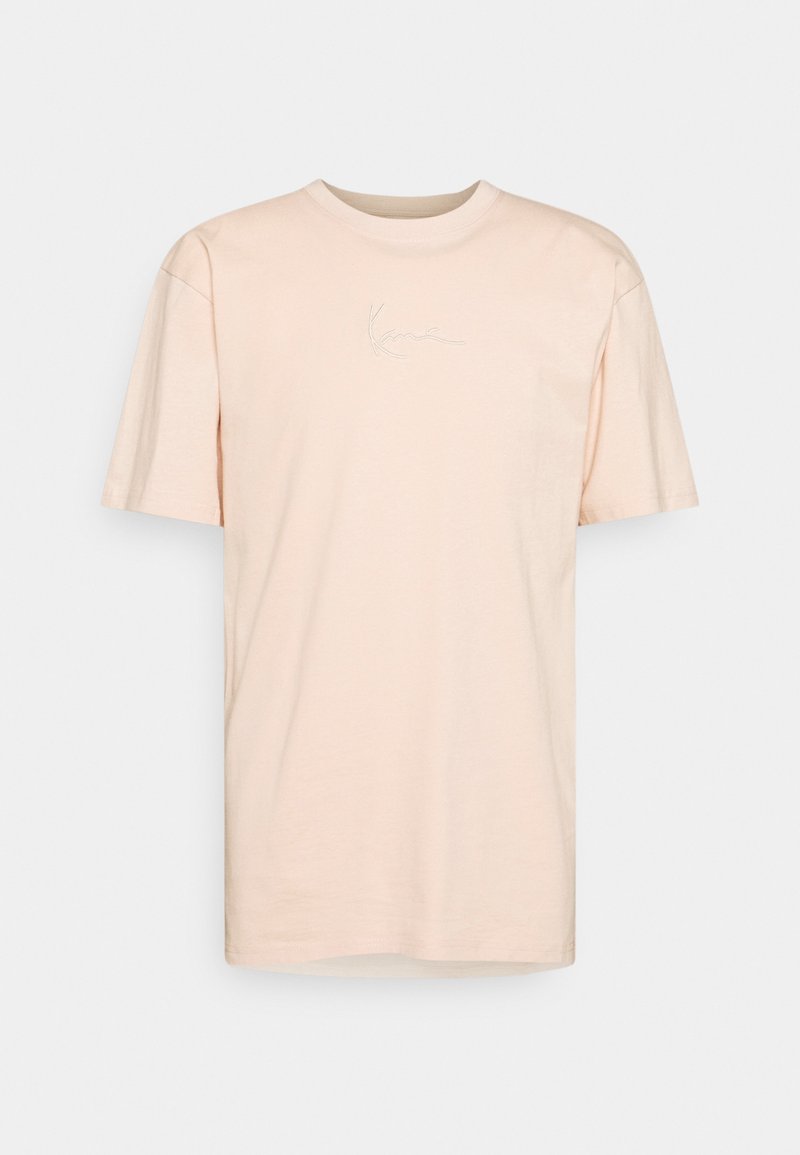 Ljus persika bomullströja med korta ärmar, rund halsringning och broderad signaturdetalj på framsidan. Slät textur, avslappnad passform.