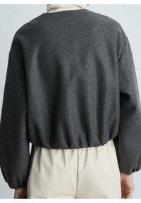 Grijze, gestructureerde sweatshirt met een geribbelde tailleband en ballonmouwen, gedragen over een lichtbeige onderstuk, dat een minimalistisch ontwerp laat zien.