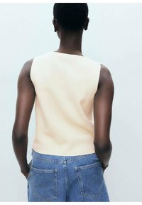 Figurbetontes ärmelloses Oberteil aus weichem Pfirsichmaterial mit glatter Textur. Kombiniert mit hochgeschnittenen blauen Denim-Shorts mit Gesäßtaschen.