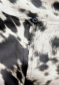 Black and white patterned fabric with a smooth texture, featuring a button and a seam along the edge of the pocket area.