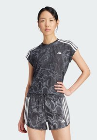 Černé sportovní tričko s krátkým rukávem, které má texturovaný, hadovitý vzor, doplněné o odpovídající šortky a bílé detaily se třemi pruhy.