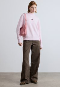 Pulover roz deschis texturat, croială lejeră, asortat cu pantaloni maro cu picioare largi și pantofi balerini cu imprimeu leopard. Accesoriile includ o geantă roz.