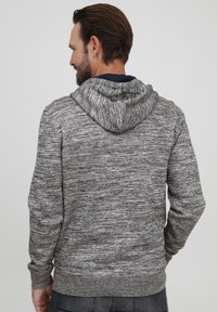 Grå melert hettegenser med strukturert strikk, med bakhette og ribbestrikkede mansjetter. Designet er avslappet med en løs passform.