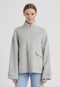 Grau gesteppte Wolljacke mit hohem Kragen, durchgehendem Reißverschluss, Fronttaschen und weiten Ärmeln, mit Knopfakzenten und einer weichen Textur.