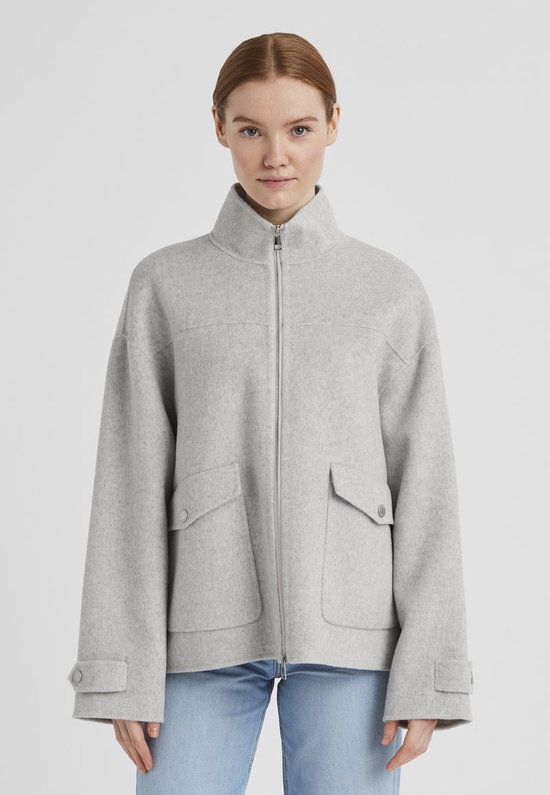 Grau gesteppte Wolljacke mit hohem Kragen, durchgehendem Reißverschluss, Fronttaschen und weiten Ärmeln, mit Knopfakzenten und einer weichen Textur.