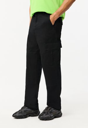 Zwarte cargo broek met zakken, gemaakt van duurzaam materiaal, met een losse pasvorm en een recht ontworpen pijp. Gecombineerd met donkere sportschoenen.