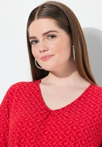 Top rojo de cuello en V con un patrón texturizado y motivos de ciervos, hecho de una tela suave, con detalle de plisado en el escote.