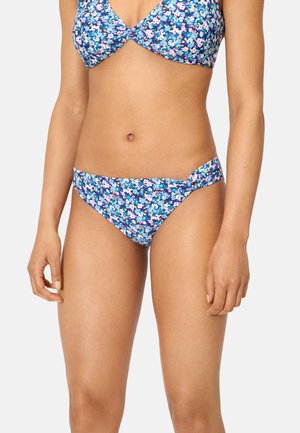 Mujer con un bikini azul floral con flores moradas, blancas y azul claro sobre un fondo sencillo.