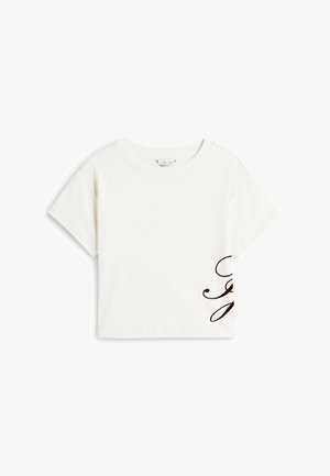 Witte kortere T-shirt met korte mouwen, gemaakt van katoen, met een vloeiende bruine scriptontwerp aan de onderzijde rechts. Ronde halslijn.