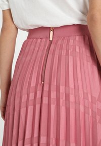 Falda plisada rosa con un diseño texturizado, cinturilla elástica y una cremallera metálica visible en la parte trasera. Acabado en tela suave.
