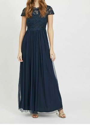 Femme portant une robe longue bleu marine avec un corsage en dentelle et des manches courtes, associée à des talons ouverts dorés.