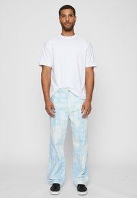White short-sleeve t-shirt paired with light blue pants featuring a diamond pattern. Black sneakers complete the outfit.