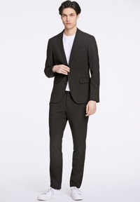 Schwarzer Anzug mit Jacke und Hose in schlanker Passform. Dazu ein weißes T-Shirt und weiße Sneakers für einen modernen Look.