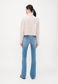 Pull en maille côtelée rose clair, design court. Associé à un jean flare bleu, texture lisse avec des détails cousus, décoloration subtile.