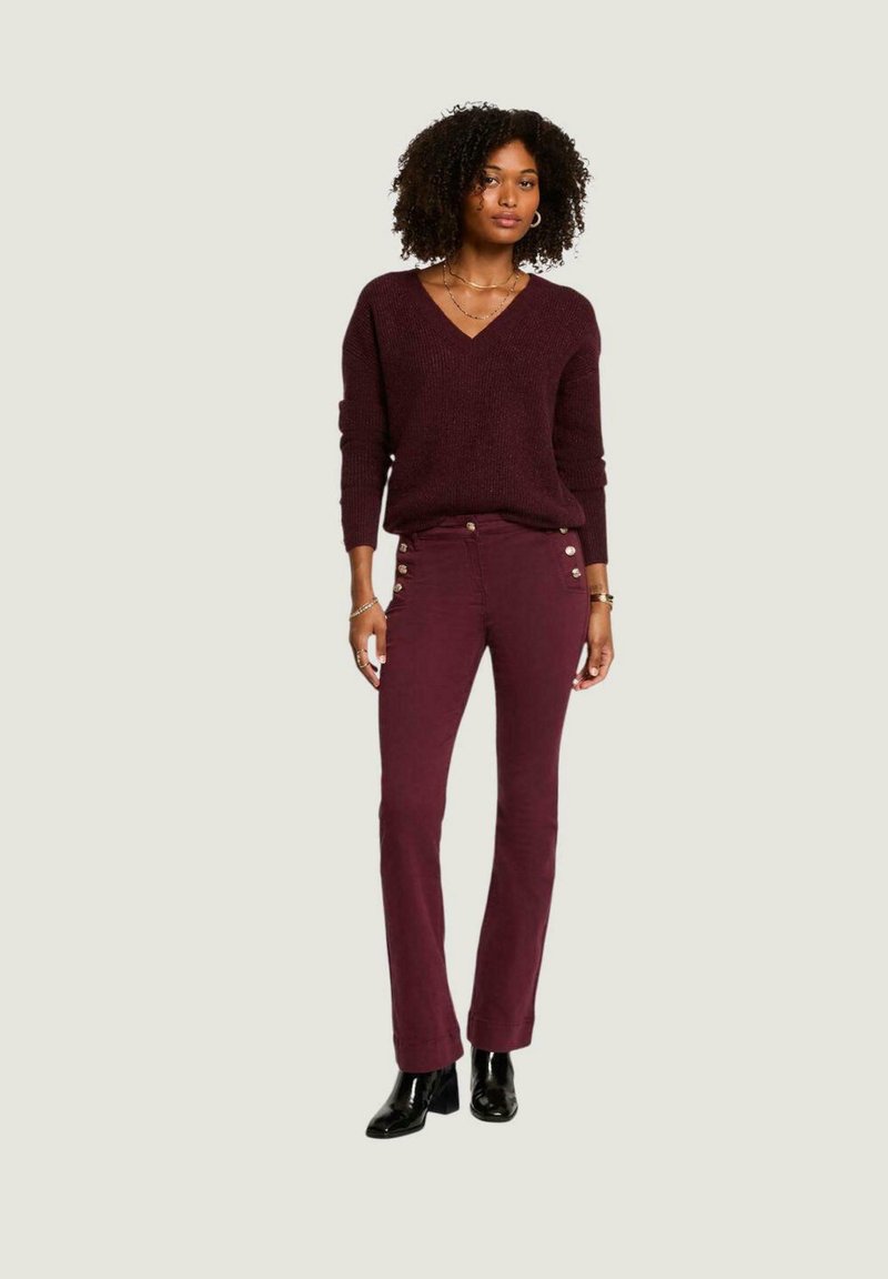 Maglione a maglia color bordeaux con scollatura a V e maniche lunghe, abbinato a pantaloni bordeaux aderenti con bottoni laterali. Indossato con tacchi neri.
