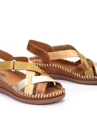 Sandalias de cuero marrón y dorado con correas cruzadas, detalles de costura y suela plana. El diseño presenta texturas y colores variados.