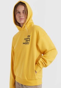 Żółta bluza z kapturem i kangurzą kieszenią oraz ściągaczami. Na piersi znajduje się czarna grafika "The Future Surf Society", wykonana z miękkiego materiału.