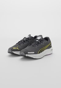 Chaussures de sport noires avec des accents jaunes, tige en maille pour la respirabilité, semelle intermédiaire rembourrée et semelle extérieure en caoutchouc texturé. Comprend des lacets et un logo.