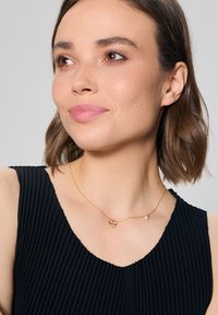 Złoty naszyjnik z łańcuchem, z zawieszką w kształcie serca i małym akcentem perły. Łańcuszek jest delikatny o subtelnej teksturze.