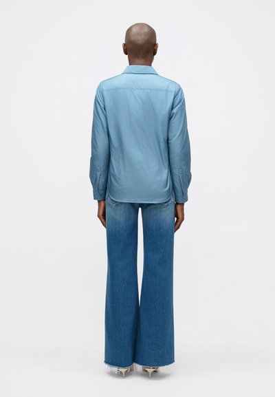 Lichtblauw overhemd met lange mouwen, gecombineerd met wijde denim jeans. Het shirt heeft een gladde textuur, terwijl de jeans een vervaagde kleur en een gerafelde zoom hebben.