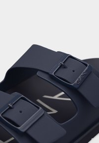 Σανδάλι σε ναυτικό μπλε με δύο ρυθμιζόμενα λουριά με αγκράφες και μερικό ορατό λογότυπο της μάρκας στην πέλμα.