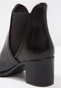 Bottine en cuir noir avec un panneau élastique texturé, un embout arrondi et un talon épais. Surface lisse avec des détails de couture minimaux.