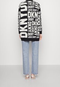 Czarny i biały sweter z powtarzającym się logo "DKNY", w połączeniu z jasnoniebieskimi dżinsami typu denim z postrzępionymi nogawkami i białymi szpilkami.