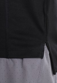 Camisa deportiva negra con una textura suave, que presenta aberturas laterales. Abajo, pantalones cortos grises tienen pequeñas perforaciones a lo largo de la tela.