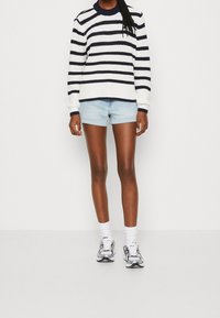 Suéter de punto a rayas blancas y marino con puños acanalados, combinado con pantalones cortos de mezclilla azul claro y zapatillas plateadas. Atuendo simple y casual.