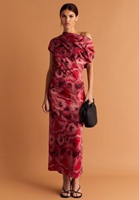 Czerwona i różowa sukienka wieczorowa tie-dye z dekoltem odsłaniającym ramiona, zwiewną sylwetką i miękkim materiałem. Połączona z czarną torebką i sandałkami na obcasie.