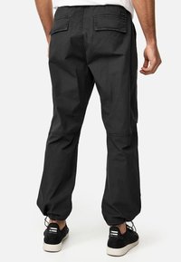 Pantalones cargo negros de algodón con un corte relajado, que cuentan con bolsillos traseros y puños elásticos en los tobillos. Combinados con zapatillas negras.