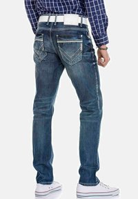 Vervagende blauwe denim jeans met een slim fit, contrasterende stiksels, twee achterzakken en een witte riem. Draagt met witte sneakers.