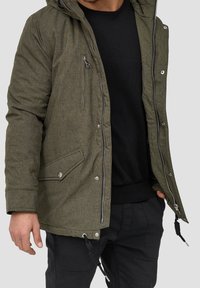 Olivgrüner, strukturiertes Außenjacke mit Kapuze, Frontreißverschluss, Druckknopf-Taschen, verstellbarem Kordelzug-Saum und gerippten Bündchen.