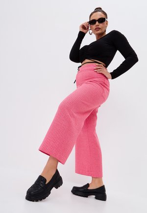 Pantaloni a gamba larga rosa testurizzati abbinati a un top nero a maniche lunghe, accessoriati con occhiali da sole neri e scarpe nere chunky.
