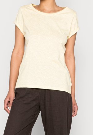 Kortærmet, lysegul t-shirt med et diskret mønster af prikker, rund halsudskæring og opkørte ærmekanter, kombineret med mørkebrune, løstsiddende bukser.