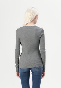 Gray long-sleeve t-shirt with a ribbed texture and a round neckline, shown from the back, paired with dark blue jeans.
