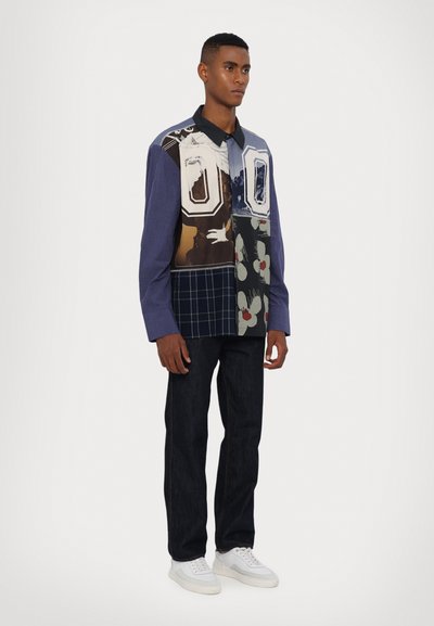 Multicolored button-up shirt with varied patterns, including florals and stripes, paired with dark jeans and white sneakers.