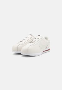 Valged nahast tennisetossud, millel on ümar varvas, minimalistlik disain ja helehall swoosh. Omavad valget tallat ja punast aksentiribaga.