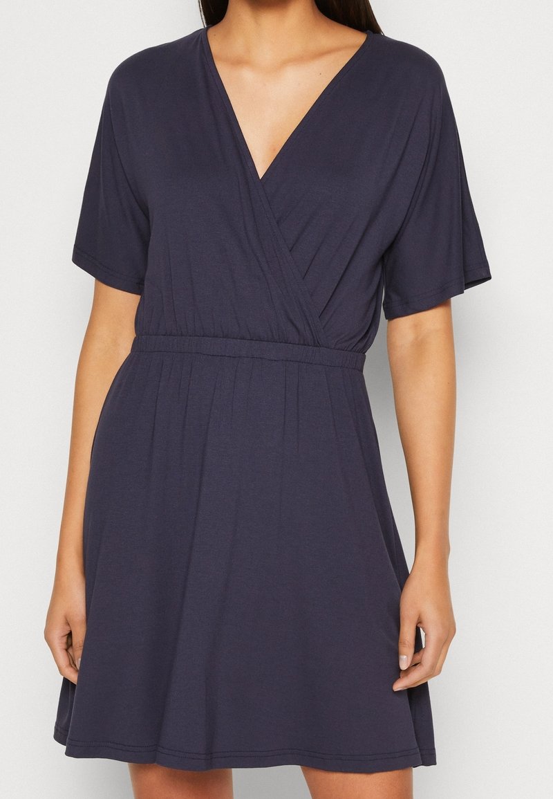 Granatowa sukienka kopertowa z krótkimi rękawami, dekoltem w serek, elastyczną talią i zwiewnym dołem. Wykonana z miękkiego materiału o gładkiej strukturze.