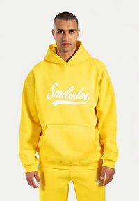 Sudadera con capucha amarilla de mezcla de algodón, con un bolsillo frontal y un logo blanco "Smilodox" en el pecho. Textura suave, ajuste relajado.