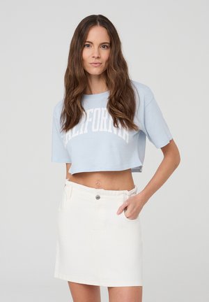 T-shirt cropped azzurro chiaro con la scritta "CALIFORNIA" stampata in bianco. Abbinato a una gonna di denim bianca con chiusura a bottoni e cintura.
